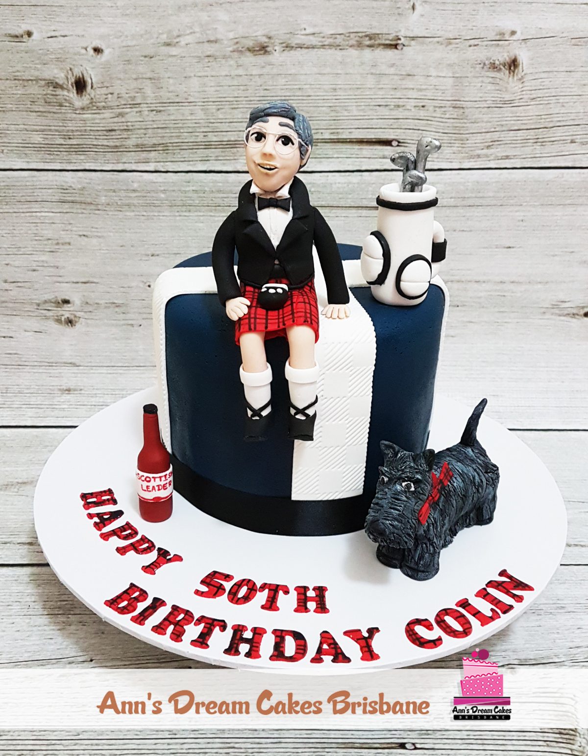 Navy and white 50th birthday cake with a fondant golfer in a kilt, golf bag and Scottie dog